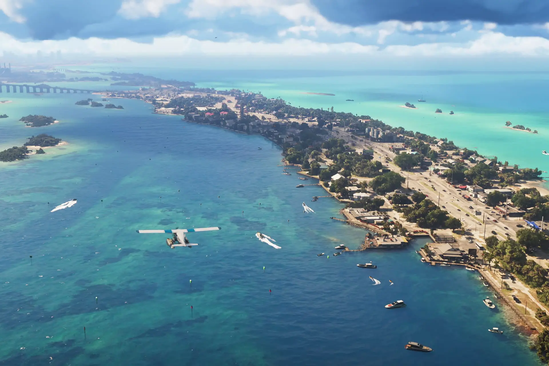 Vista aérea de una localidad costera con una hidroavión flotando sobre aguas turquesa, barcos cerca y un puente largo al fondo.